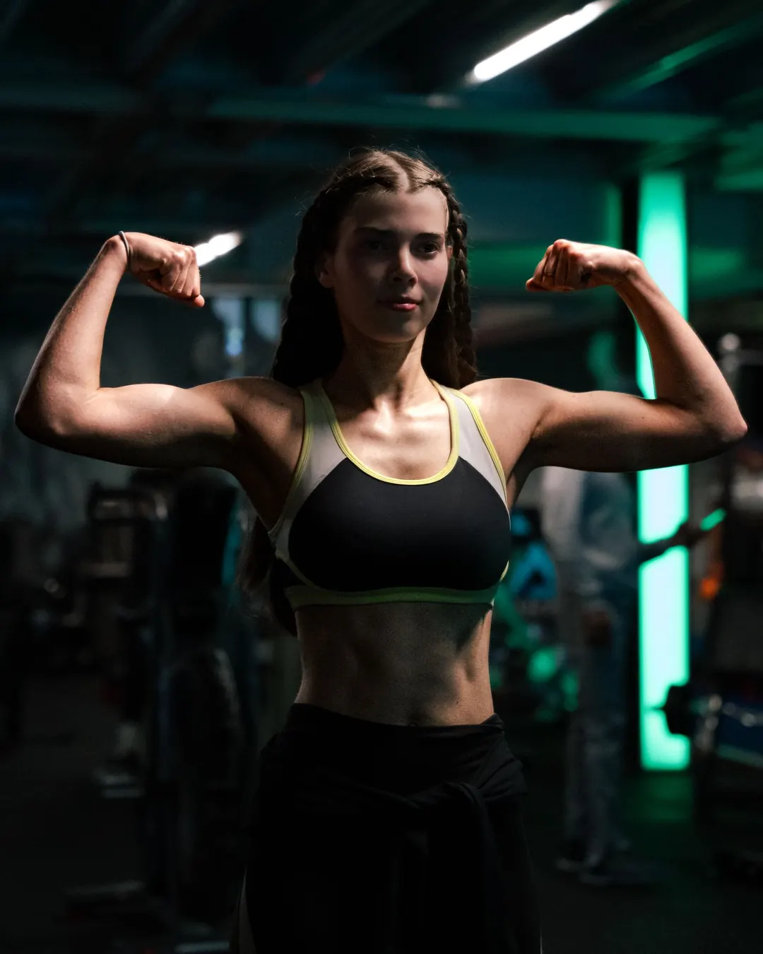 Une sportive contracte ses biceps dans une salle de sport éclairée au néon.